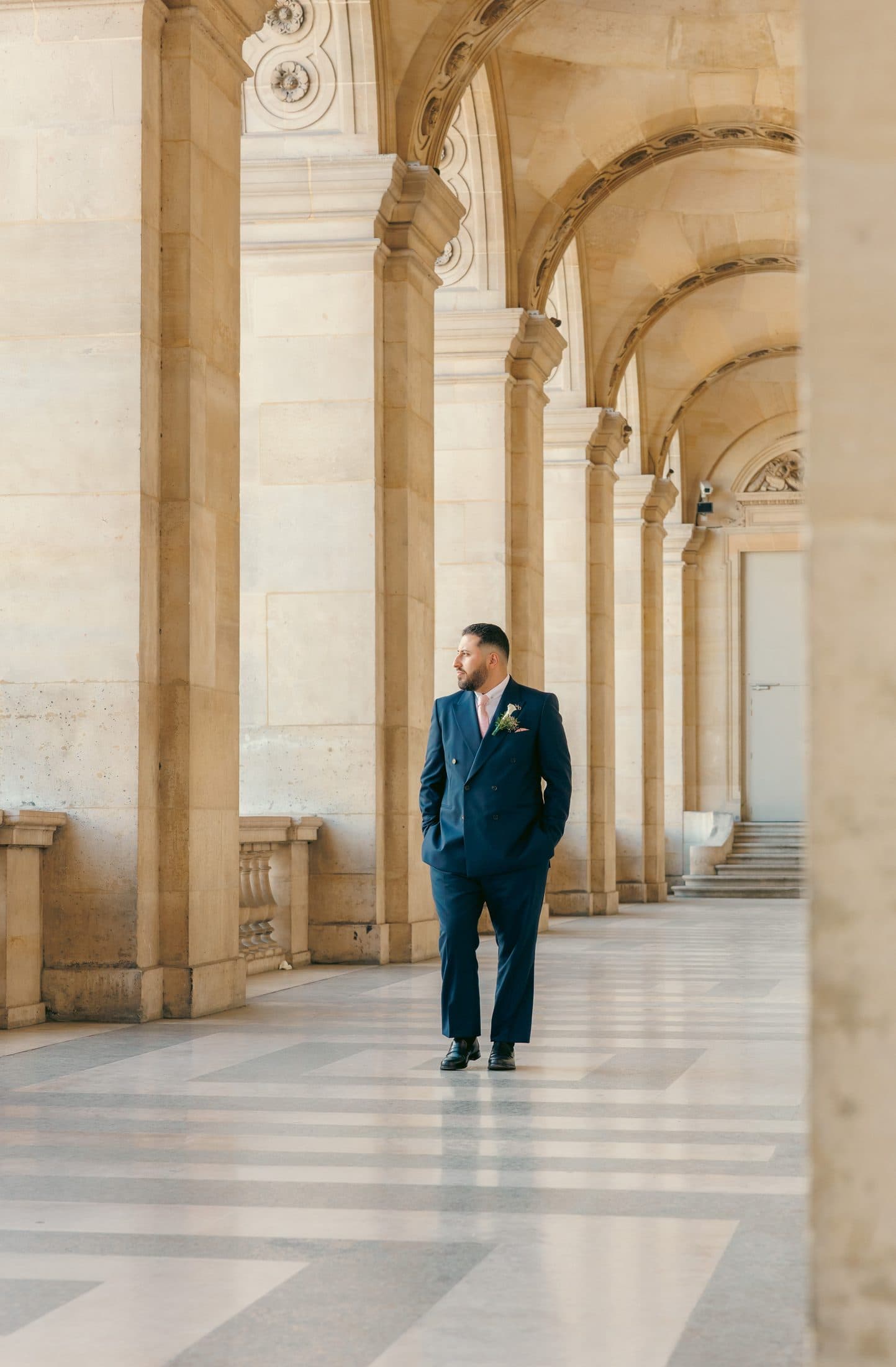 Marié en costume bleu marine sous les arcades dorées du Louvre