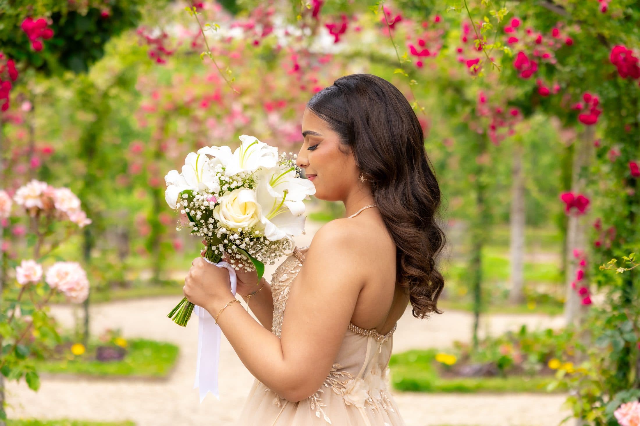 Mariée respirant son bouquet sous une arche de roses
