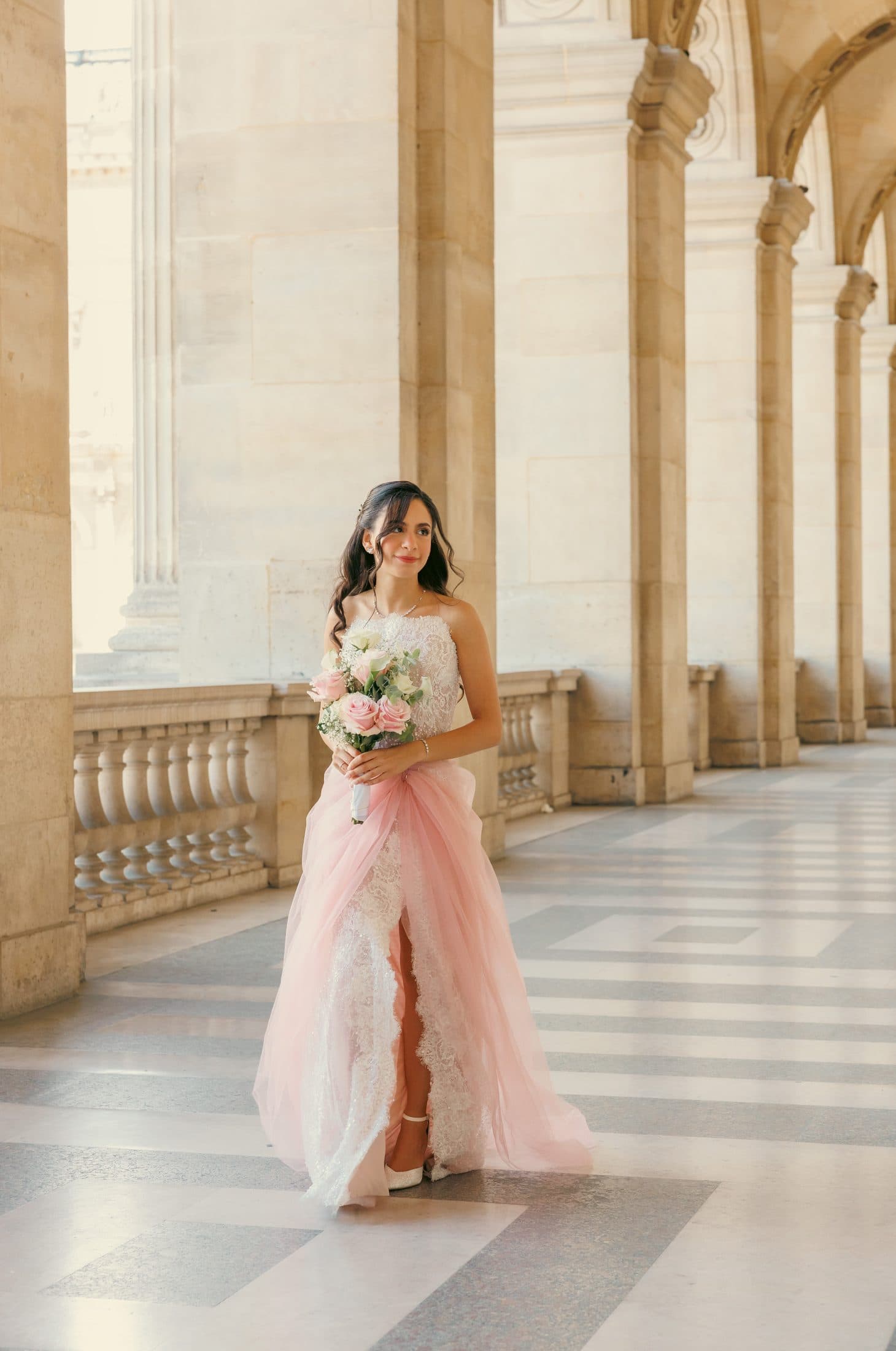 Mariée en robe rose poudré sous les arcades du Louvre à Paris